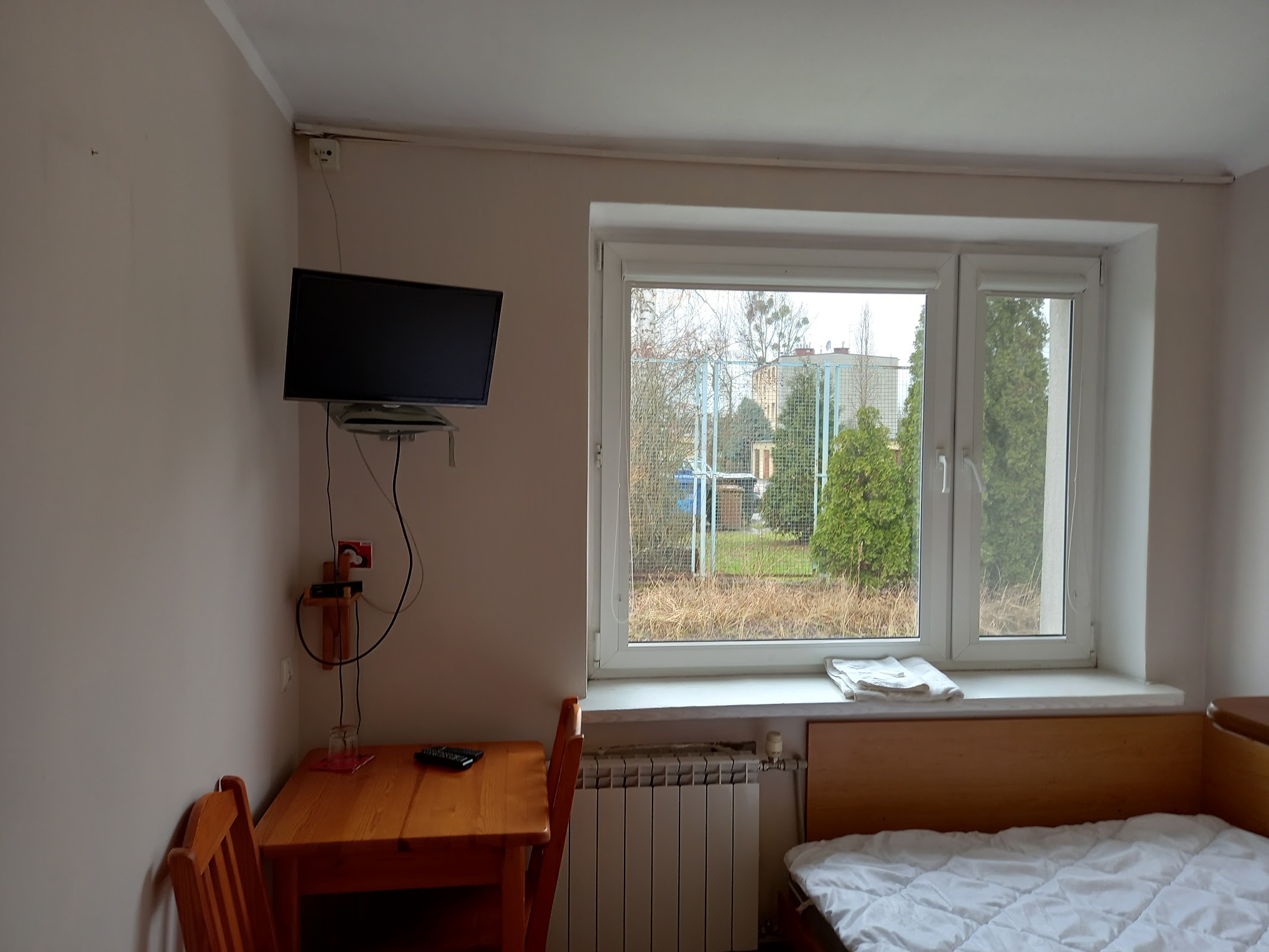 Pokój gościnny w Zajeździe Tymianek - jasna ściana, telewizor na ścianie, drewniane biurko z krzesłem, okno z widokiem na zieleń, łóżko po prawej